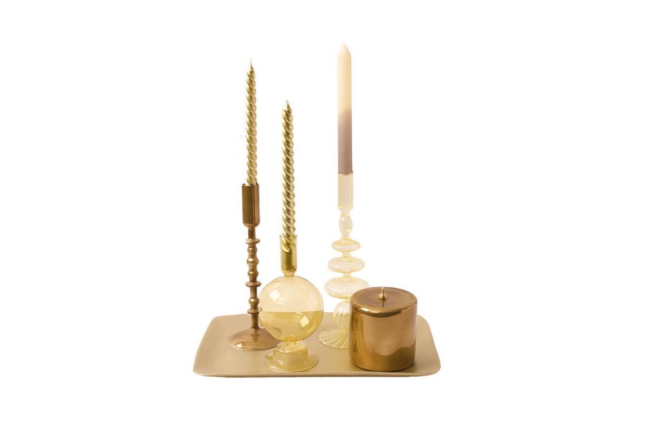3 verschillende kandelaren en een olielamp in de kleuren goud en geel op een schaal