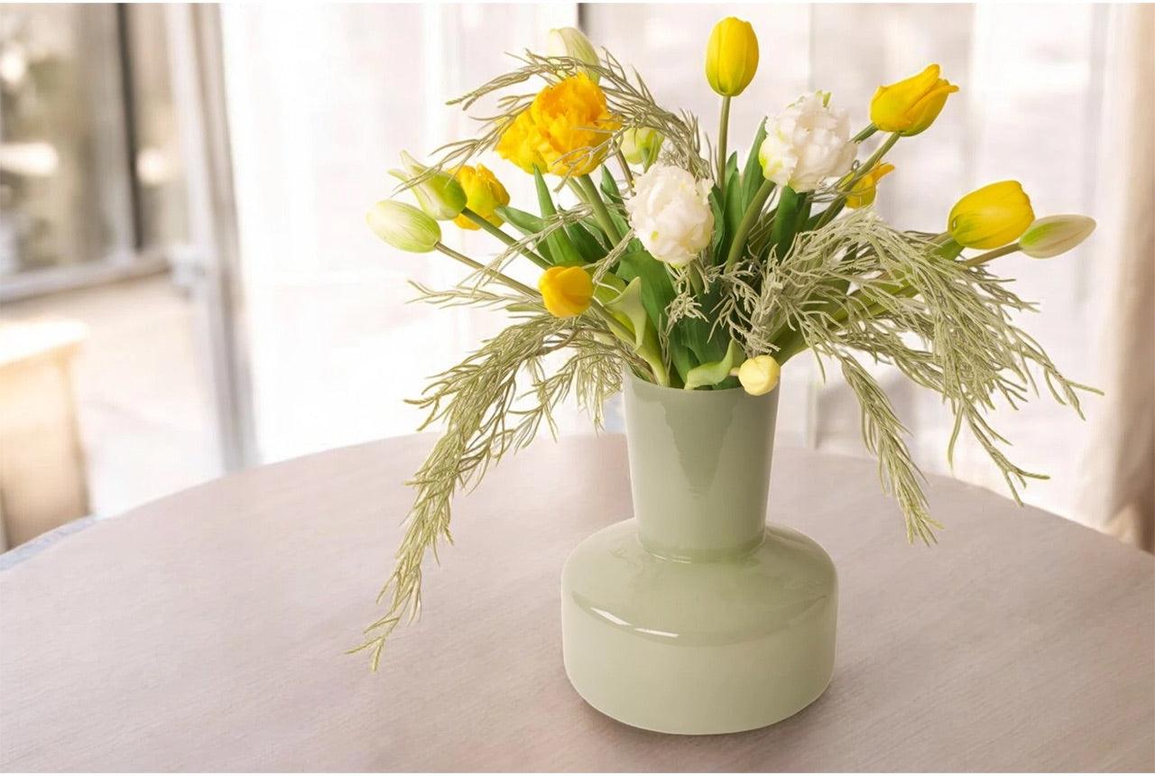 Kunsttulpen als boeket gebonden met gele en witte parkiettulpen en tulpen op een groene glasvaas als sfeer op een tafel voor het raam- WinQ