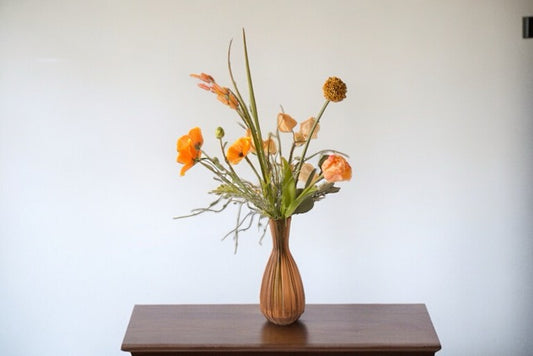 kunstbloemen boeket in oranje kleuren op een bruine tafel voor een witte muur