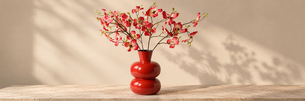 Een rode metalen vaas met ringen met kunstbloemen op een tafel voor een muur - WinQ