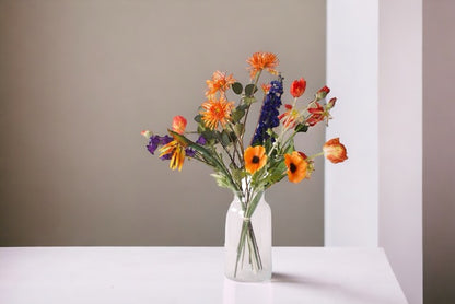 Kunstbloemen Veldboeket Rood/ Blauw/ Oranje inclusief Glasvaas op witte tafel tegen taupe kleurige muur
