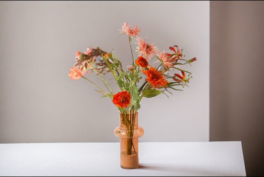 Veldboeket Zijden Bloemen Rood/ Roze/ Oranje inclusief vaas op een witte tafel met een witte en bruine muur
