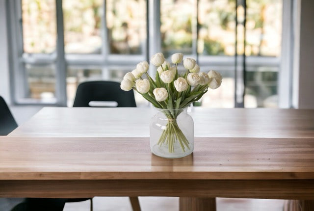 Kunstboeket witte tulpen  in een glasvaas op een houten tafel voor het raam
