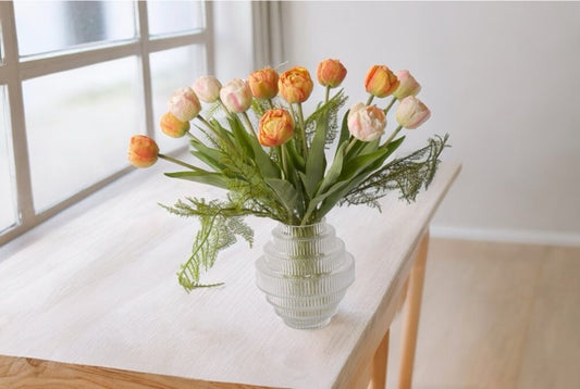Oranje en roze tulpen in een bolle glasvaas op een tafel voor het raam