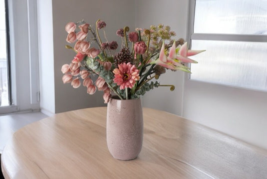 Veldboeket kunstbloemen in de diverse kleuren mauve en roze op een houten tafel voor een raam