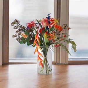 Veldboeket kunstbloemen bloemen in de kleurcombinatie Blauw, Rood, Oranje met diverse soorten bloemen op een houten tafel voor het raam