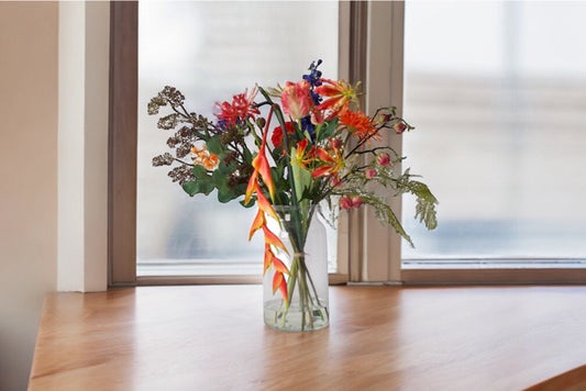 Veldboeket kunstbloemen bloemen in de kleurcombinatie Blauw, Rood, Oranje met diverse soorten bloemen op een houten tafel voor het raam