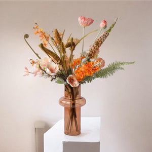 Veldboeket kunstbloemen bloemen in de kleurcombinatie Zalm en Oranje op een witte zuil voor een lichte hoek met een raam