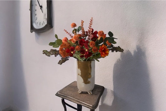 Boeket kunstblinden op een parelmoer vaas. Bloemen in de kleur rood en oranje met onder andere Tulp, Cosmea, Schermbes en Gerbera op een houten tafeltje voor een lichte muur