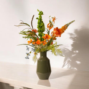 Kunstbloemen boeket met vaas in hoogglans groen in een oranje arrangement op een lichte tafel 