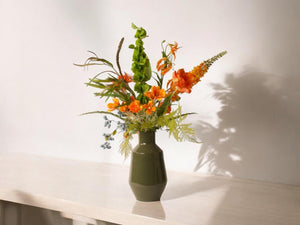Kunstbloemen boeket met vaas in hoogglans groen in een oranje arrangement op een lichte tafel 