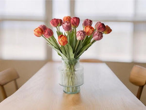 Boeket kunsttulpen  in de kleuren rood, mauve en warm oranje in een glasvaas op een houten tafel voor een raam - WinQ