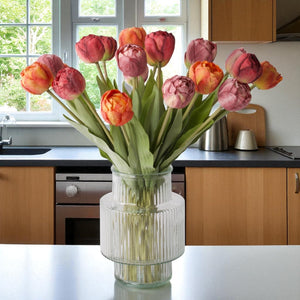 Boeket kunsttulpen  in de kleuren rood, mauve en warm oranje in een glasvaas op een tafel in de keuken voor een raam - WinQ