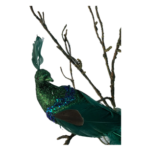 Decorative glittery green peacock perched on bare branch with detailed feathers