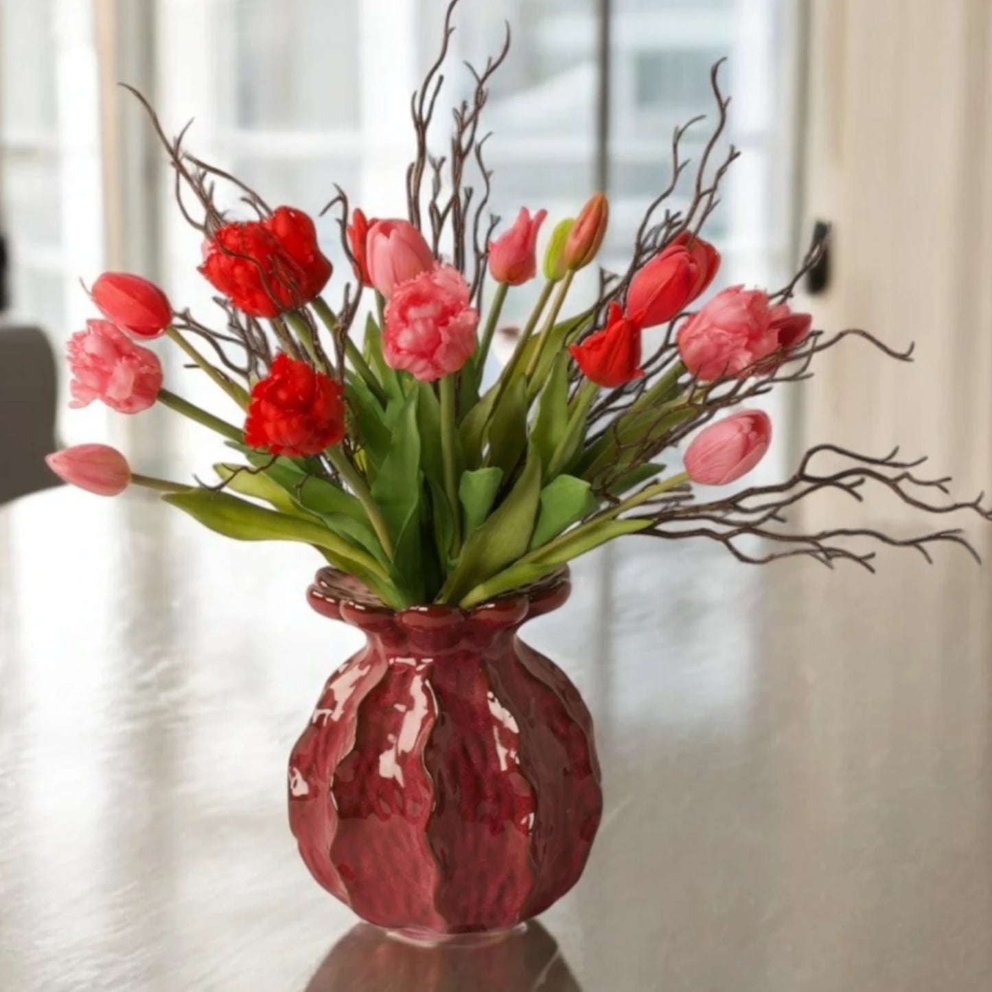 boeket parkiet kunsttulpen in rood en pink gebonden met twijgen in een rode keramieken vaas op een tafel voor het raam - WinQ