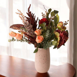 Arrangement van gebonden zijden bloemen in bordeaux en oud roze op een keramieken vaas op een houten tafel -WinQ