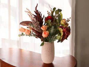 Arrangement van gebonden zijden bloemen in bordeaux en oud roze op een keramieken vaas op een houten tafel -WinQ