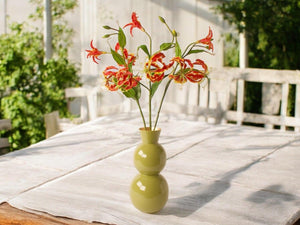 3 kunsttakken van de gloriosa in de kleur rood op een groene vaas op een houten tafel -WinQ