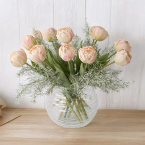 boeket van roze tulpen met bladgroen in een bolle glasvaas op een houten tafel voor een witte muur - WinQ