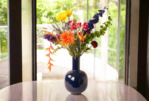 Grote vaas in een glanzende donker blauwe kleur maat 26x40cm met kunstbloemen boeket op een tafel voor het raam- WinQ