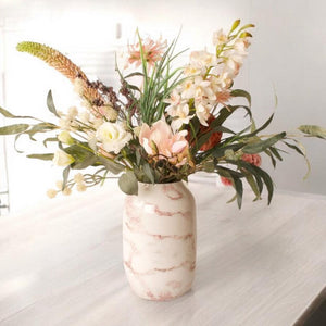 Boeket kunstbloemen in de kleuren roze ne wit op een hooglans metalen vaas met marmer motief op een witte tafel
