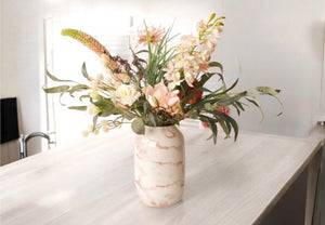 Boeket kunstbloemen in de kleuren roze ne wit op een hooglans metalen vaas met marmer motief op een witte tafel