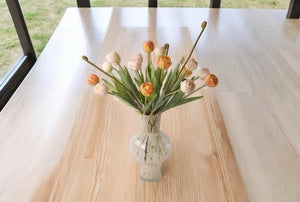 Boeket met kunsttulpen 7 oranje en 7 licht roze kunsttulpen in een glasvaas met een witte tekening in het glas  op een houten tafel voor het raam 