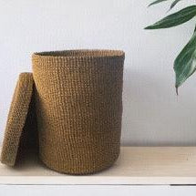 Opbergmand Abaca 25x35cm Beige met deksel op een witte plank aan een witte muur en een groene plant in een pot
