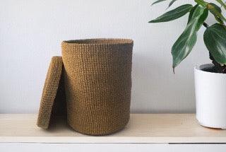 Opbergmand Abaca 25x35cm Beige met deksel op een witte plank aan een witte muur en een groene plant in een pot