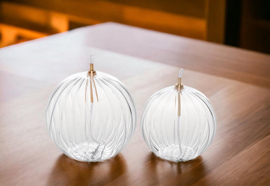 Set Olielamp van helder glas Olielamp diameter 10 en 12cm van helder glas met een verticale ribbelstructuur inclusief lont en houder op een houten tafel