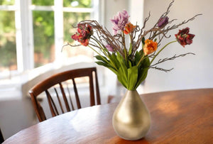 Gouden vaas met papagaai kunsttulpen in rood, oranje, lila en paars gebonden met verschillende twijgen in een gouden vaas op een houten tafel - WinQ