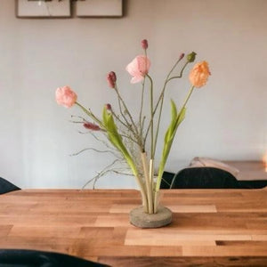 Kunsttulpen, papaver en grassen in een Pijpvaas Goud op een houten tafel met een lichte muur