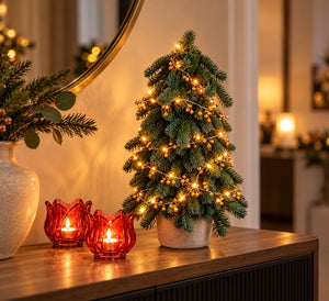 sfeervolle foto van een kerstboom 40cm hoog van WinQ inclusief sfeervolle belletjes en verlichting op batterij op een sidetable met 2 kleine rode waxinehouders van WinQ