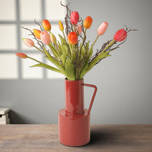 Sfeerfoto van een ebonden boeket met 15 tulpen in oranje roze en pink gecombineerd met bremtakjes op een rode metalen vaas met handvat op een houten tafel - WinQ