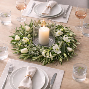 Sfeervolle eettafel met groene kunstbloemenkrans, witte bloemen en kaars als centerpiece.