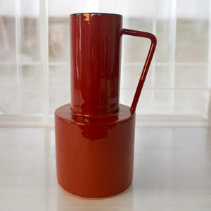 rode vaas metaal met een handvat op een lichte tafel - WinQ