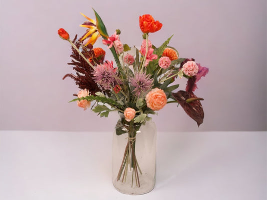 Gebonden veldboeket kunstbloemen in de kleuren oranje paars  en roze combinatie in een vaas van helder glas