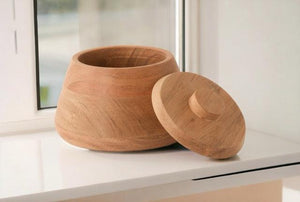 Voorraadpot van Acaciahout met een deksel diameter onder 15cm en hoogte 11cm op een plank voor  het raam