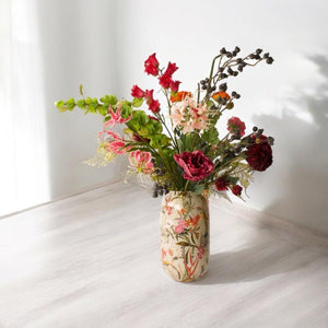 Kunstbloemenboeket met diverse kunstbloemen waaronder onder andere hibiscus en gloriosa op een metalen vaas met bloemmotief op een houten keukentafel
