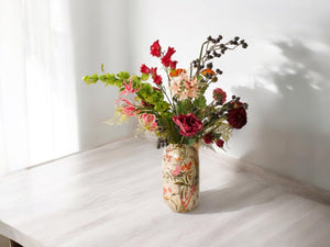 Kunstbloemenboeket met diverse kunstbloemen waaronder onder andere hibiscus en gloriosa op een metalen vaas met bloemmotief op een houten keukentafel