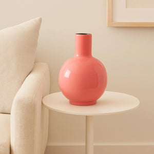 Bolvormige vaas metaal in fuchsia met diameter 23cm uitlopend aan de bovenzijde met een diamater van 7,5cm. Hoogte is 30cm op een houten tafel voor het raam - WinQ