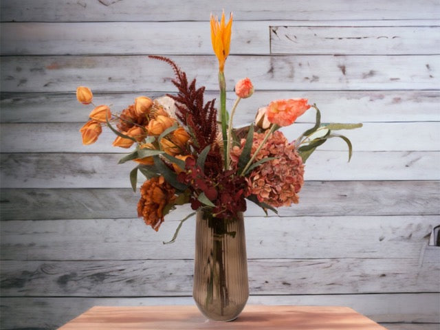 Veldboeket met oranje en rood kleuren met diverse bloemen waaronder lampion en hortensia  op een bruine glasvaas gedecoreerd op een houten tafel voor een grijze muur