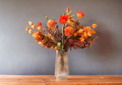 Boeket blomen 65cm hoog in een terra oranje kleurcombinatie op een glazen vaas op een houtentafel