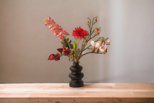 Boeket voorjaar kunstbloemen in rood/ roze combinatie met onder andere magnolia, tulpen en cymbidium  gepresenteerd op houten tafel voor een lichte muur