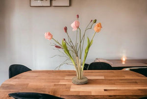Kunsttulpen, papaver en grassen in een Pijpvaas Goud op een houten tafel met een lichte muur