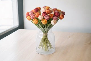 Boeket kunstbloemen tulpen in 5 kleuren totaal 35 stuks in 5 voorjaarskleuren op een vaas op een tafel voor een raam