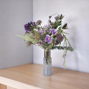 PlukBoeket Kunstbloemen Lila en Blauw op een tafel in een hoek tegen een lichte muur,.