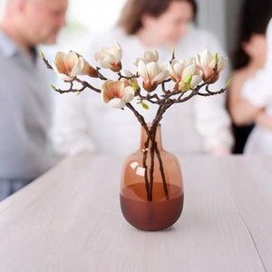 Kunstbloemen Magnolia 3 takken zacht roze inclusief vaas cognac op een tafel met een familie op de achtergrond