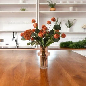 Gebonden kunstbloemen Boeket In Oranje metTulp warm Oranje Eucalyptus Zinnia Oranje Scherm oranje in een heldere cognac kleurige glasvaas op een houten eettafel in de keuken voor het aanrecht