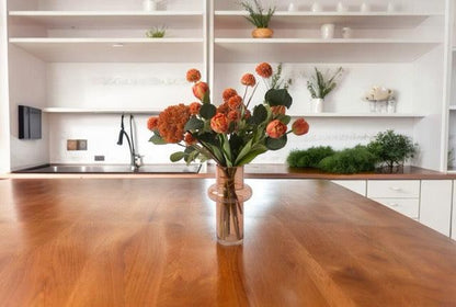 Gebonden kunstbloemen Boeket In Oranje metTulp warm Oranje Eucalyptus Zinnia Oranje Scherm oranje in een heldere cognac kleurige glasvaas op een houten eettafel in de keuken voor het aanrecht